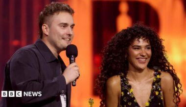 Sam Fender and Olivia Dean speaking and smiling on stage at the Brit Awards