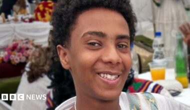 A young boy with short dark curly hair smiling at the camera.