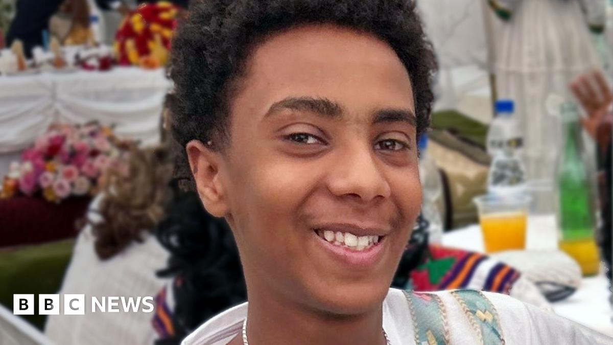 A young boy with short dark curly hair smiling at the camera.