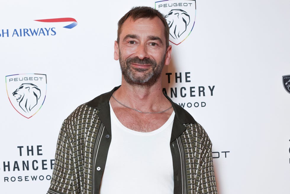 charlie condou in a patterned shirt and white tank top at event with branded backdrop