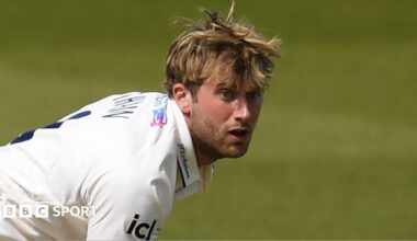 Essex cricketer Noah Thain, who is in a white Essex Cricket jersey, reacts as he bowls during a County Championship match.