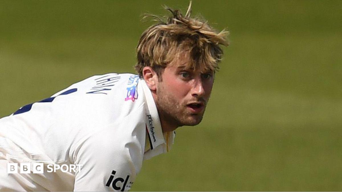Essex cricketer Noah Thain, who is in a white Essex Cricket jersey, reacts as he bowls during a County Championship match.