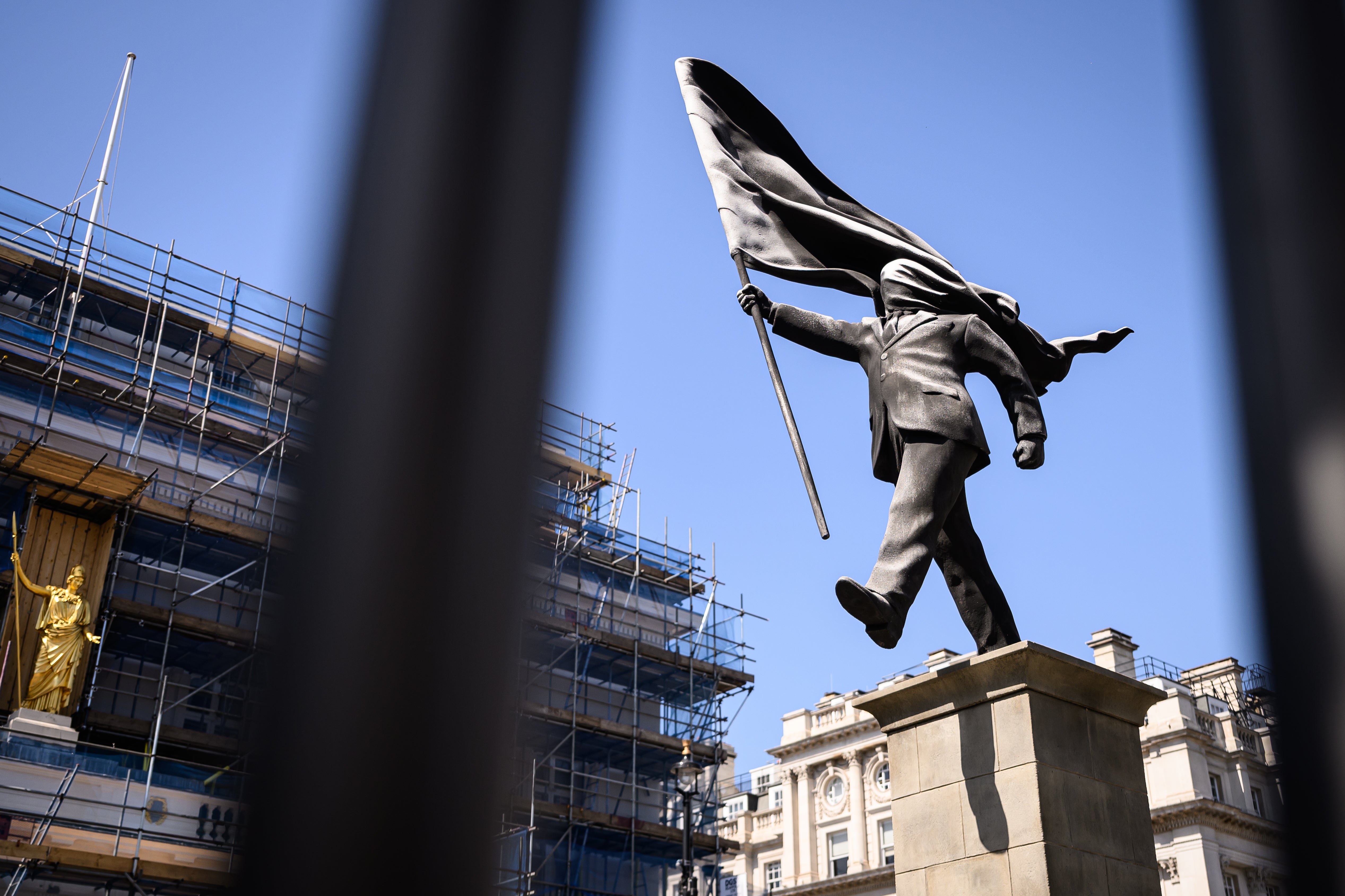 A statue by Banksy depicting a person walking from a plinth, his face covered by a billowing flag, in Waterloo Place in May