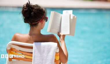 Young woman sitting in a chair with a towel draped over the back, reading at the pool in the summer