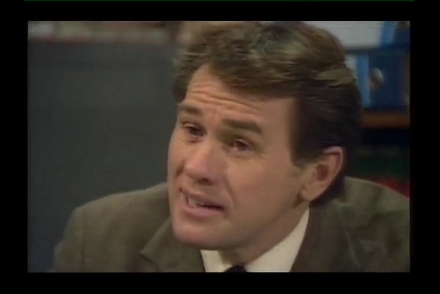A dark haired man in a brown jacket.