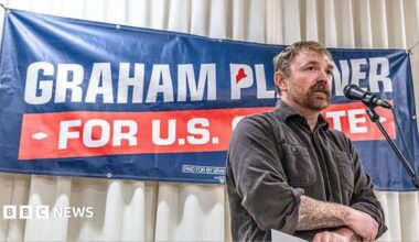 Graham Platner stands in front of a sign for his candidacy