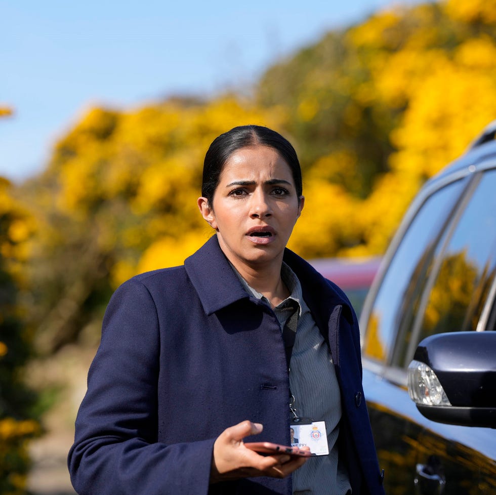 person standing beside a car, holding a phone, with yellow flowers in the background. person standing beside a car, holding a phone, with yellow flowers in the background.