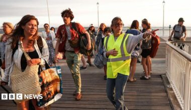 A volunteer gives indication to holidaymakers from Lege-Cap-Ferret upon their arrival in Arcachon by boat during an evacuation operation of the entire Cap-Ferret peninsula, in southwestern France, on July 24, 2026 whilst a wildfire is spreading across the area