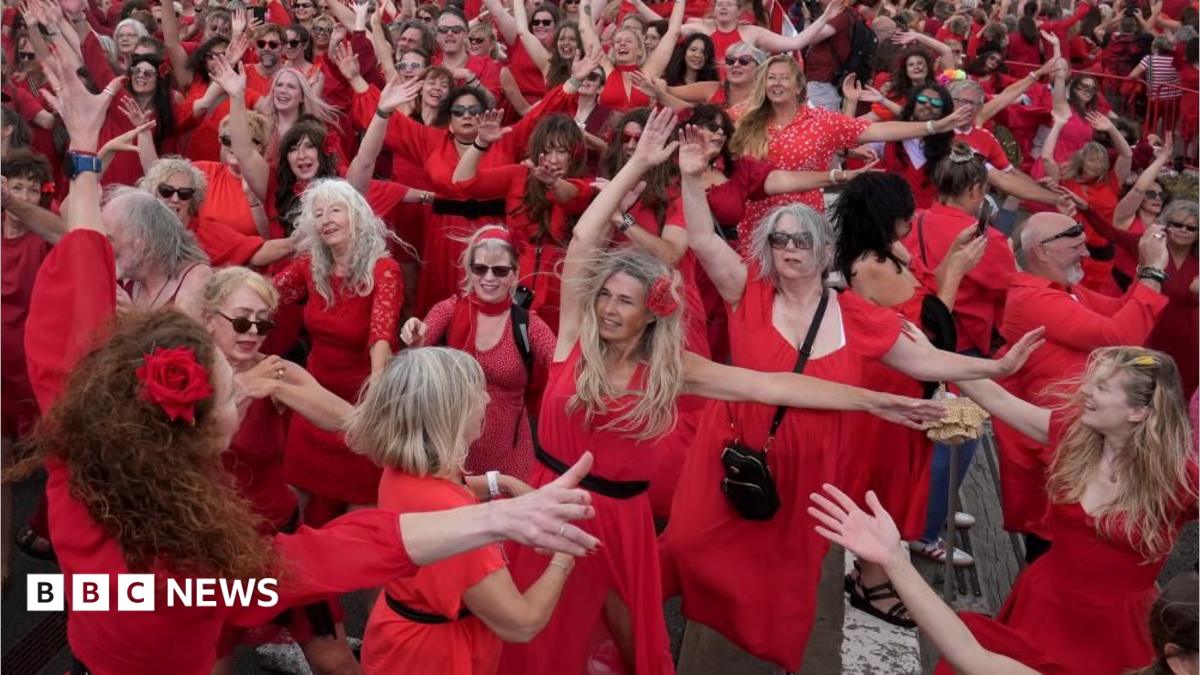 A group of people in red dresses dance with their arms in the air.