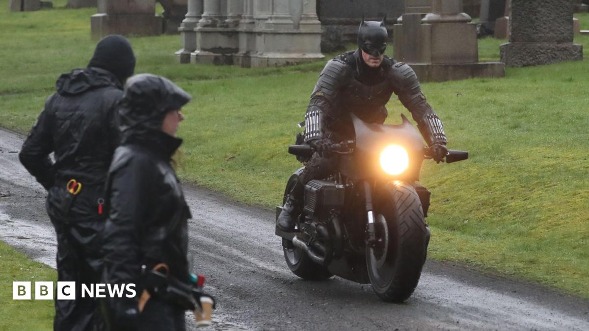 Filming on a scene in The Batman - a man dressed in a Batman costume is riding a motorbike in a graveyard, watched by crew members
