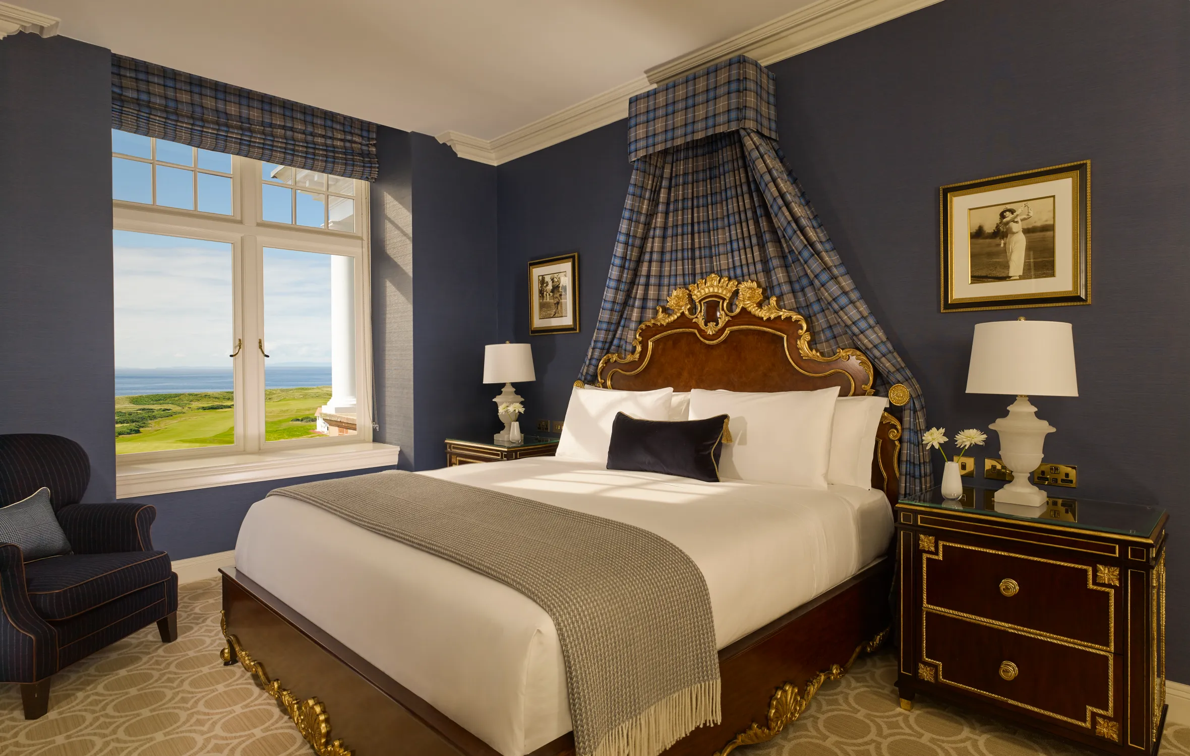 A luxurious bedroom at Trump Turnberry with a large window overlooking a golf course and the ocean.