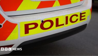 Stock image showing the rear bumper of a police car with POLICE in red lettering on a yellow hi-vis background.