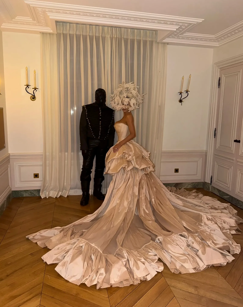 Bianca Censori made a dramatic fashion statement in a skintight cream satin corset with a detachable silk train and oversized feathered headpiece during Kanye West's birthday celebration at the Palace of Versailles.