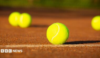 A clay tennis court with a number of bright yellow balls scattered about
