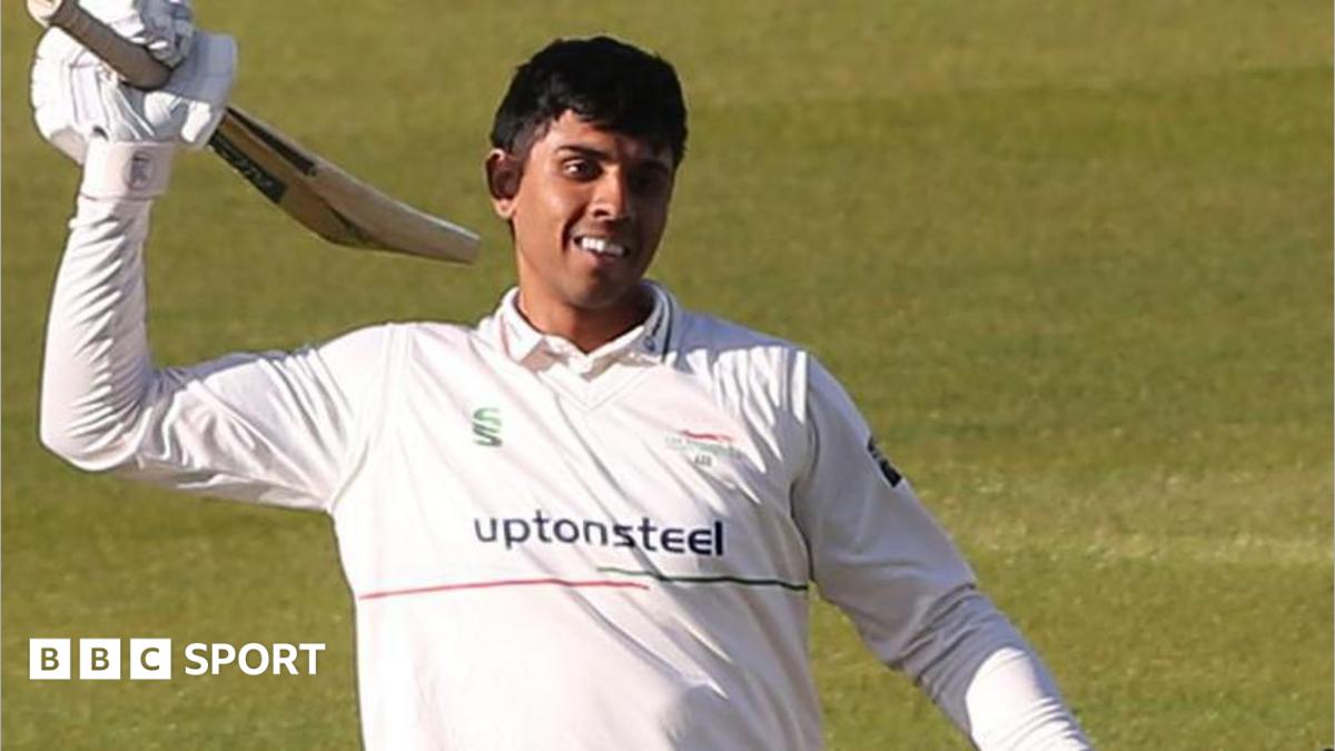 Rishi Patel wearing cricket whites celebrates scoring a century by raising his bat