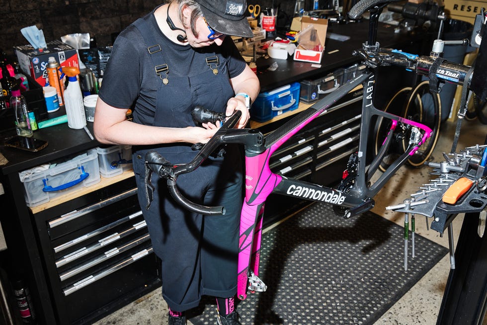 A person adjusting the handlebars on a Cannondale bicycle in a workshop with various tools and supplies nearby.