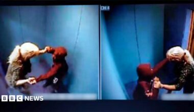 Woman with long blonde hair tied in a pony tail with a boy wearing a red hooded top inside a blue padded room.