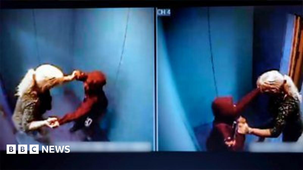 Woman with long blonde hair tied in a pony tail with a boy wearing a red hooded top inside a blue padded room.