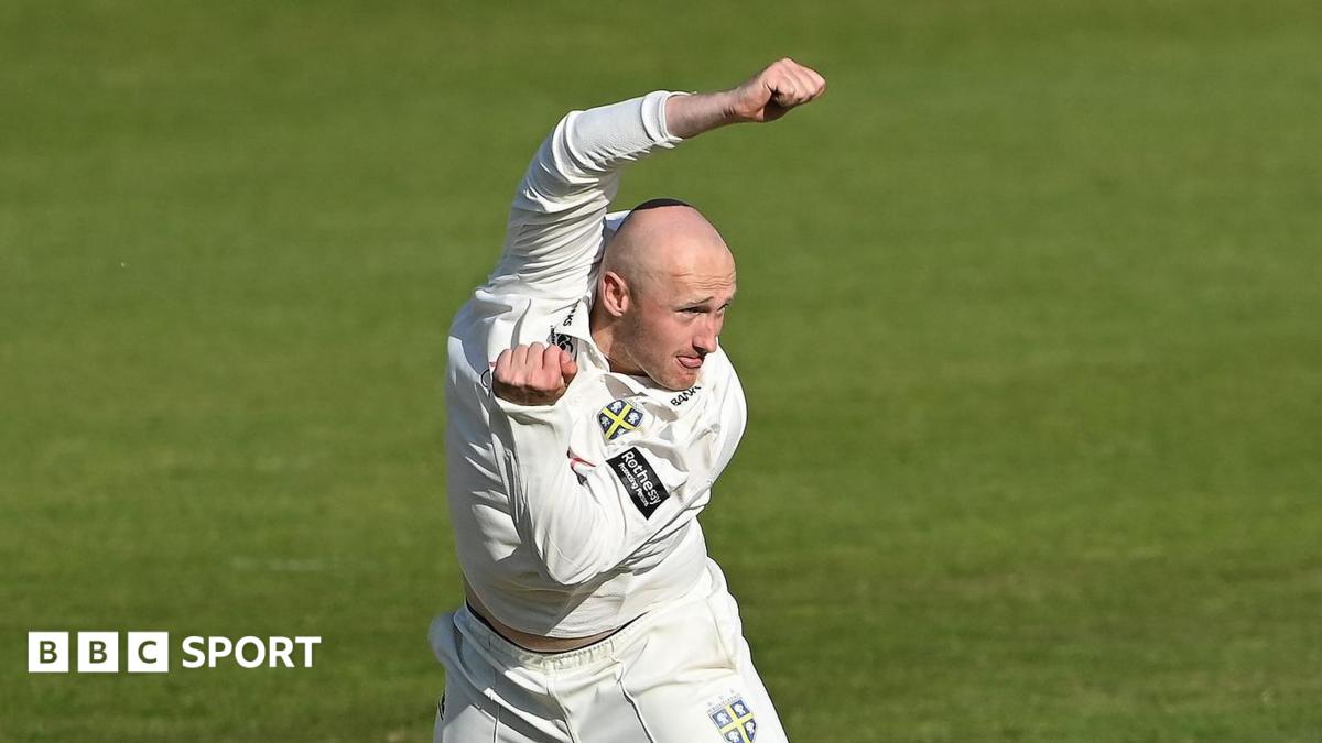 Left-arm spin bowler Callum Parkinson just after completing a delivery with his left arm tucked in and his right arm raised over his head