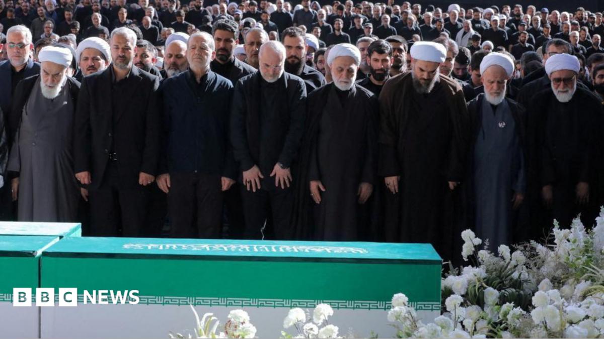 Iranian President Masoud Pezeshkian, Iran's Parliament speaker Mohammad Baqer Qalibaf and Chief Justice of Iran Gholam-hossein Mohseni Ejei with officials attend a prayer during a public farewell ceremony to pay their respects to late Supreme Leader Ayatollah Ali Khamenei. A large crowd can be seen in the background as everyone stands looking at the coffin