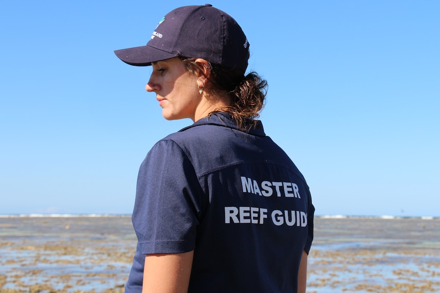 A woman wearing a navy polo with 'master reef guide' on the back with the ocean behind her