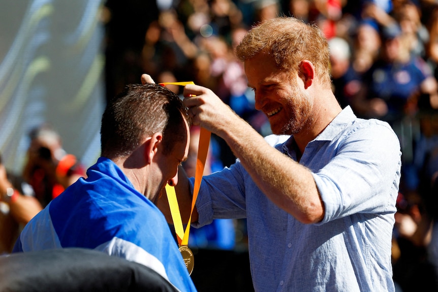 A man wearing a blue shirt puts a medal around the neck of a man facing him in a blue and white tracksuit.