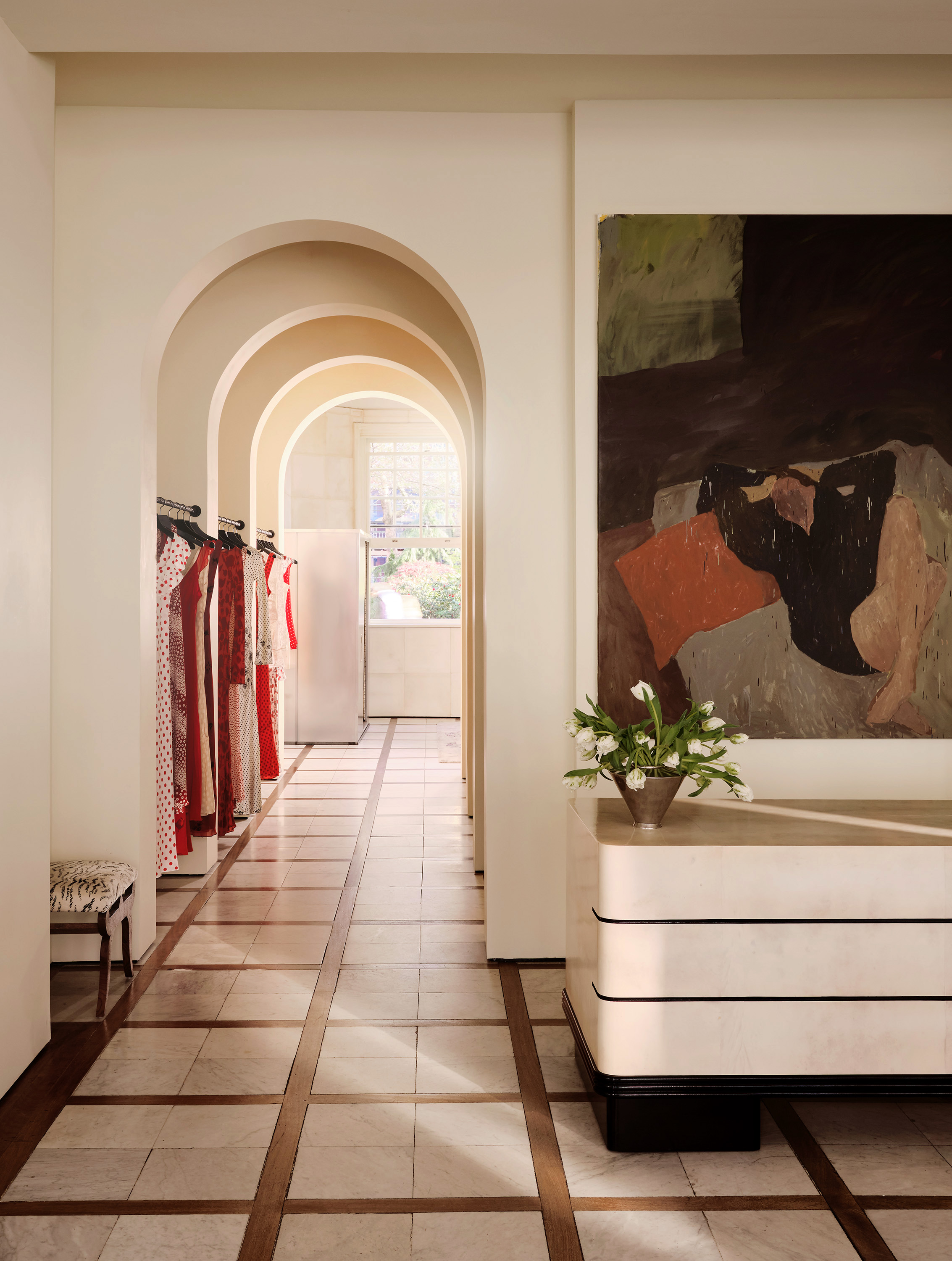 The glossy, curated interiors of a fashion boutique inspired by Italian design and architecture, with marble surfaces, statement chandeliers, and artsy separes interspersed with eye-catching clothing.