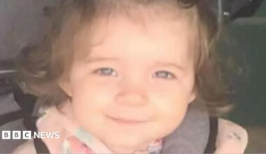 Head-and-shoulders image of Isabelle Rose Welsh. She is a two-year-old girl, is smiling directly into the camera and has dark curly hair. She is wearing a pink top.