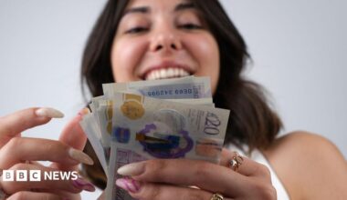 Smiling woman looks at a wad of banknotes with the camera looking from below.