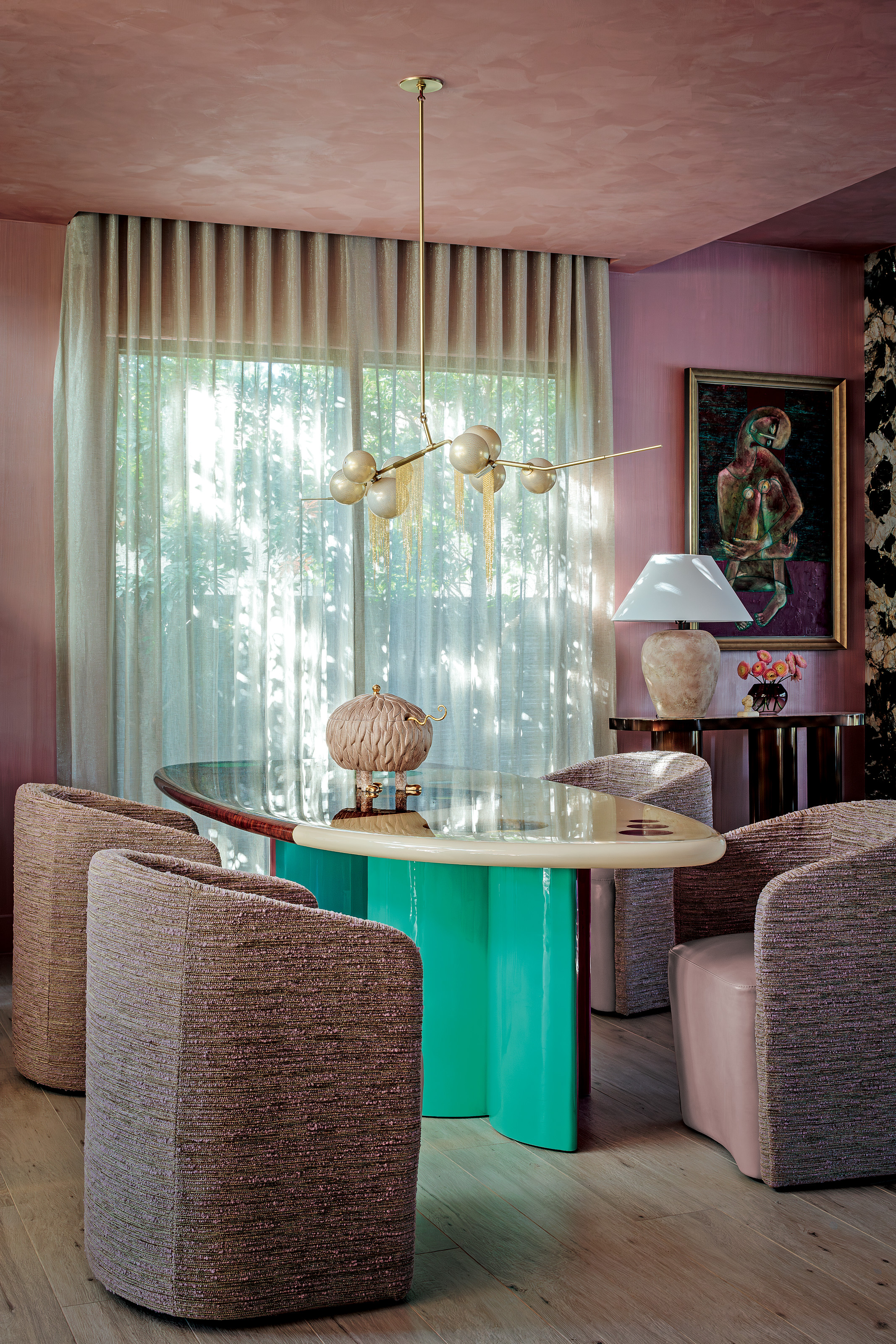 Dining area with teal, burgundy and white lacquer dining table, pink tub armchairs, globe chandelier and pink textured walls