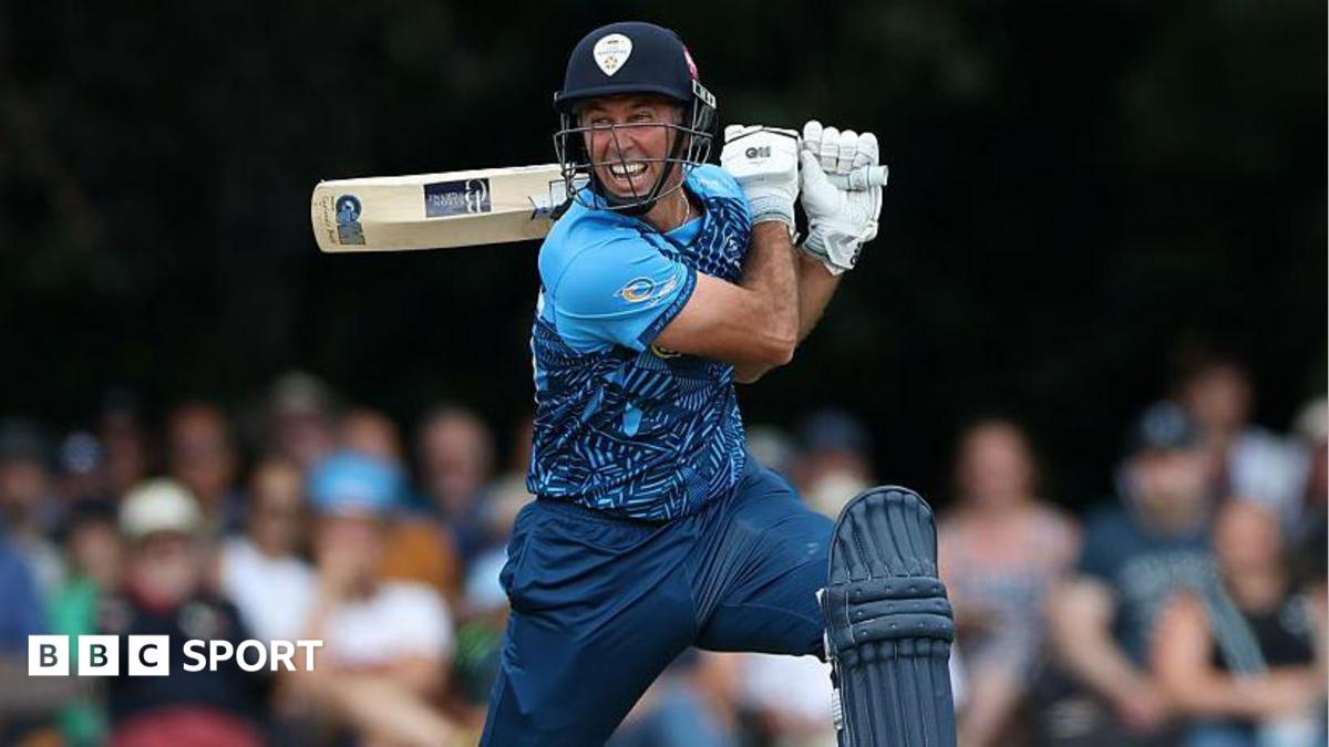 Wayne Madsen in blue Derbyshire Falcons kit holds his bat horizontally behind his head after playing a shot