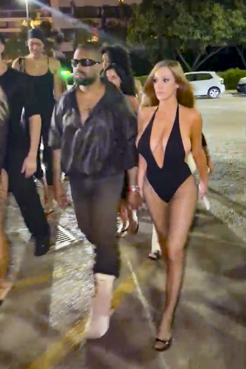 Bianca Censori and Kanye West arrive hand-in-hand at a nightclub in Ibiza, Spain, with Censori wearing a black ultra-plunging halter bodysuit layered over fishnet tights.