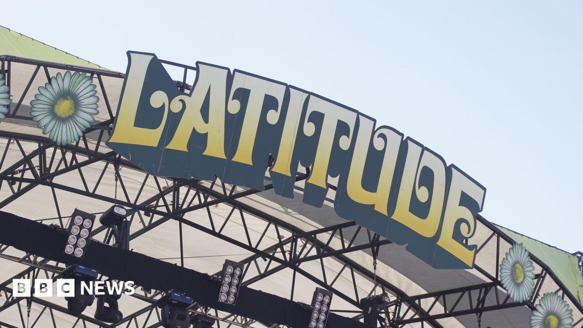 A close-up of the Latitude Festival sign on the top of a stage at the event. The letters are in block capitals, edged in black and coloured yellow fading to cream. Above it is sky.