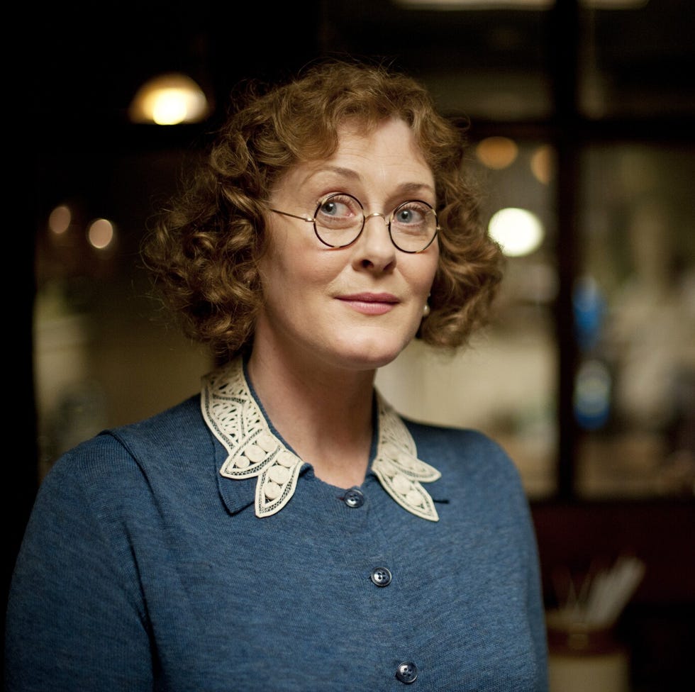 person with curly hair and glasses wearing a blue top with lace collar