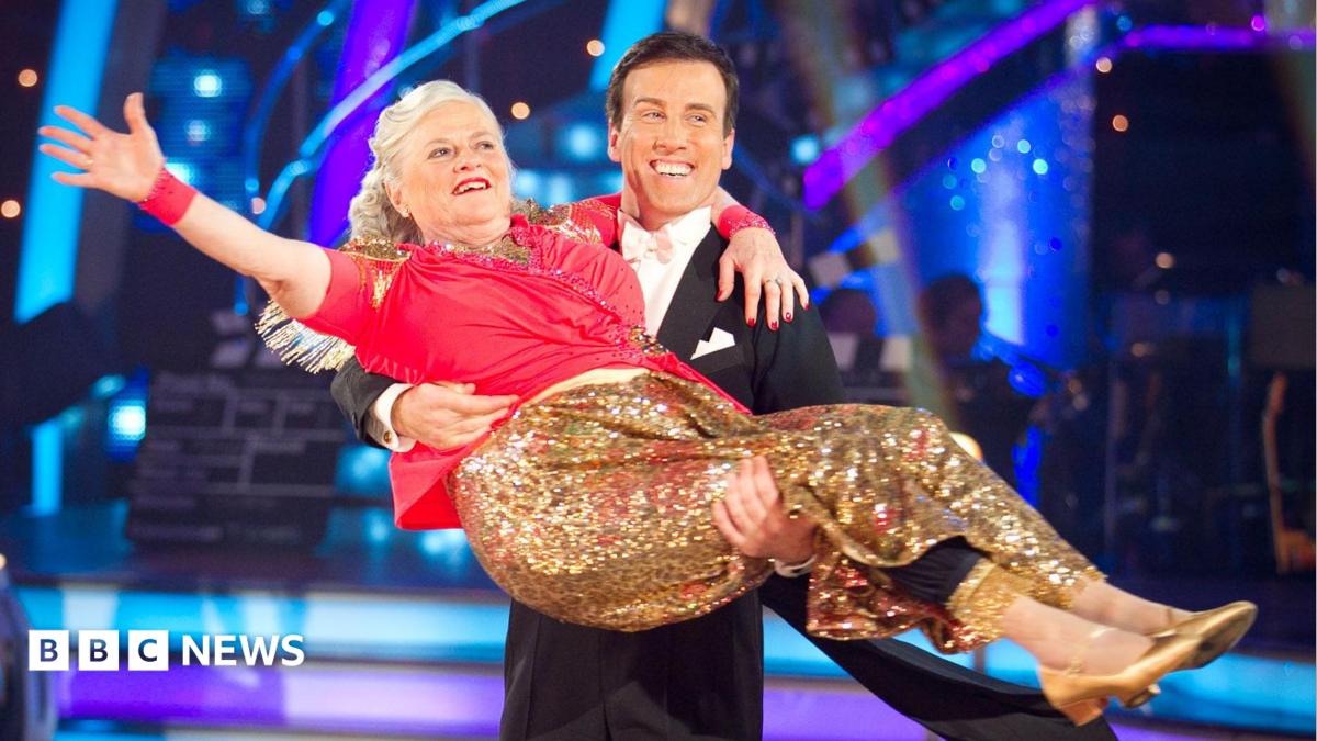 Ann Widdecombe wearing a red top and a golden glittery skirt, being held by Anton Du Beke in a tuxedo