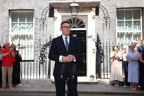 Andy Burnham standing outside 10 Downing Street. In front of him are some microphones and behind him is a small crowd of clapping people