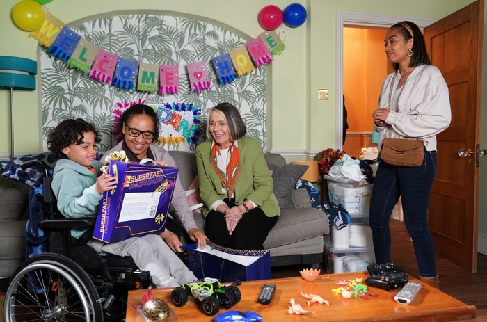 564829,TITLE:Eastenders Chelsea stands over Sheila, Libby and Jordan, who is opening a toy, in a scene from EastEnders