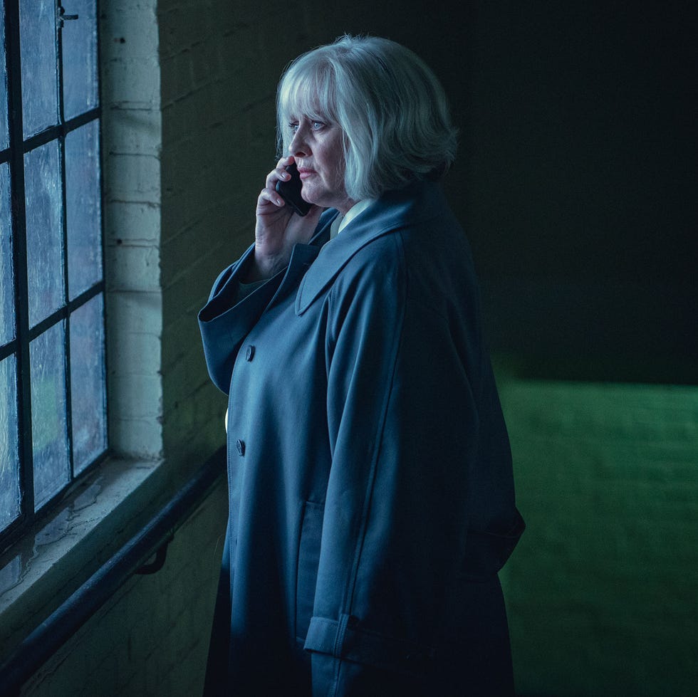 a woman making a phone call while standing near a window in a dimly lit environment