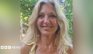 A smiling Lynn Knapp outside by a tree. Her blonde hair is down.