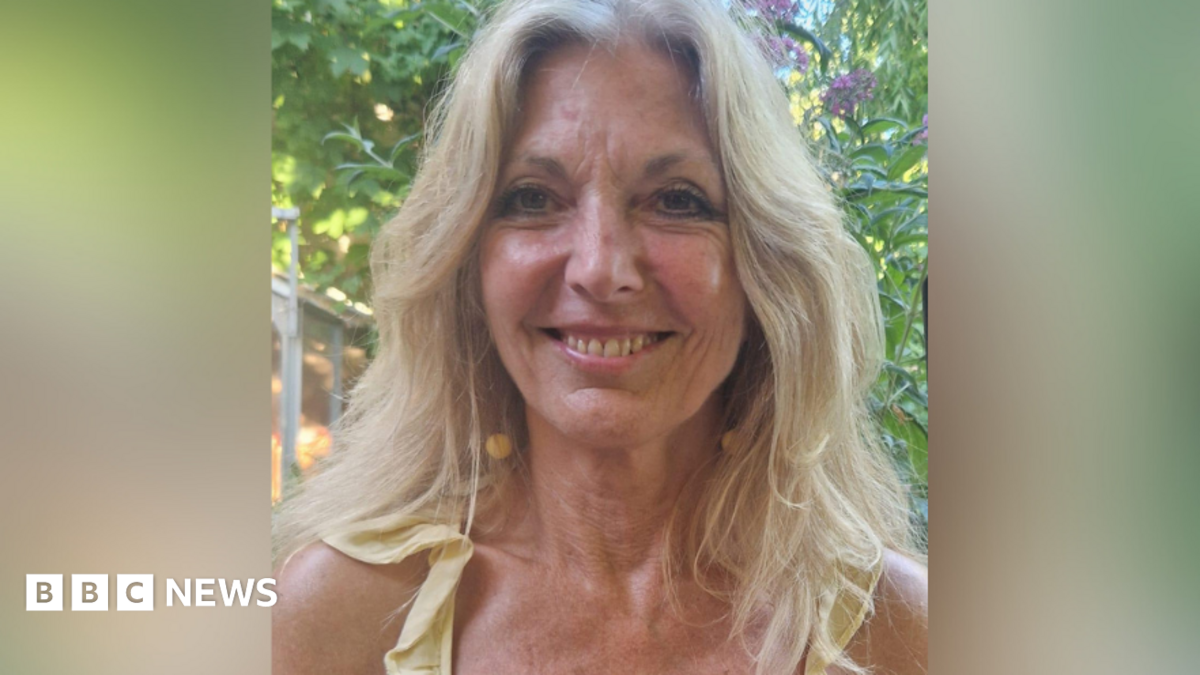 A smiling Lynn Knapp outside by a tree. Her blonde hair is down.