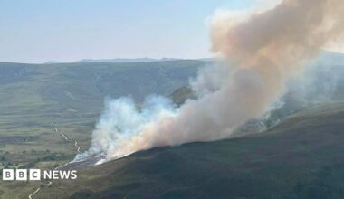 A green hill landscape with plumes of white smoke billowing into the air
