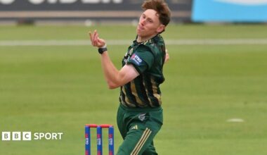 James Hayes, in green and gold kit, bowling alongside blue stumps with red bails