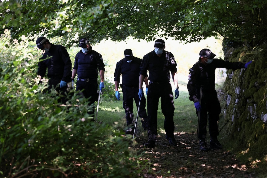 Five British police officers inspect a shaded pathway in the English countryside.