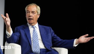 Nigel Farage wearing a blue suit and light blue patterned tie. He is sitting on a white chair.