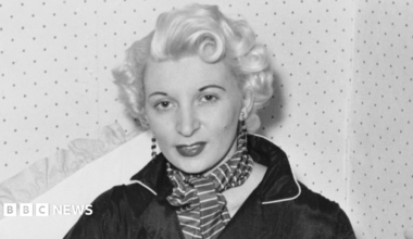 Ruth Ellis poses for a photograph - the black and white picture shows her with white-blonde hair, wearing long earrings, a striped scarf and a black shirt.