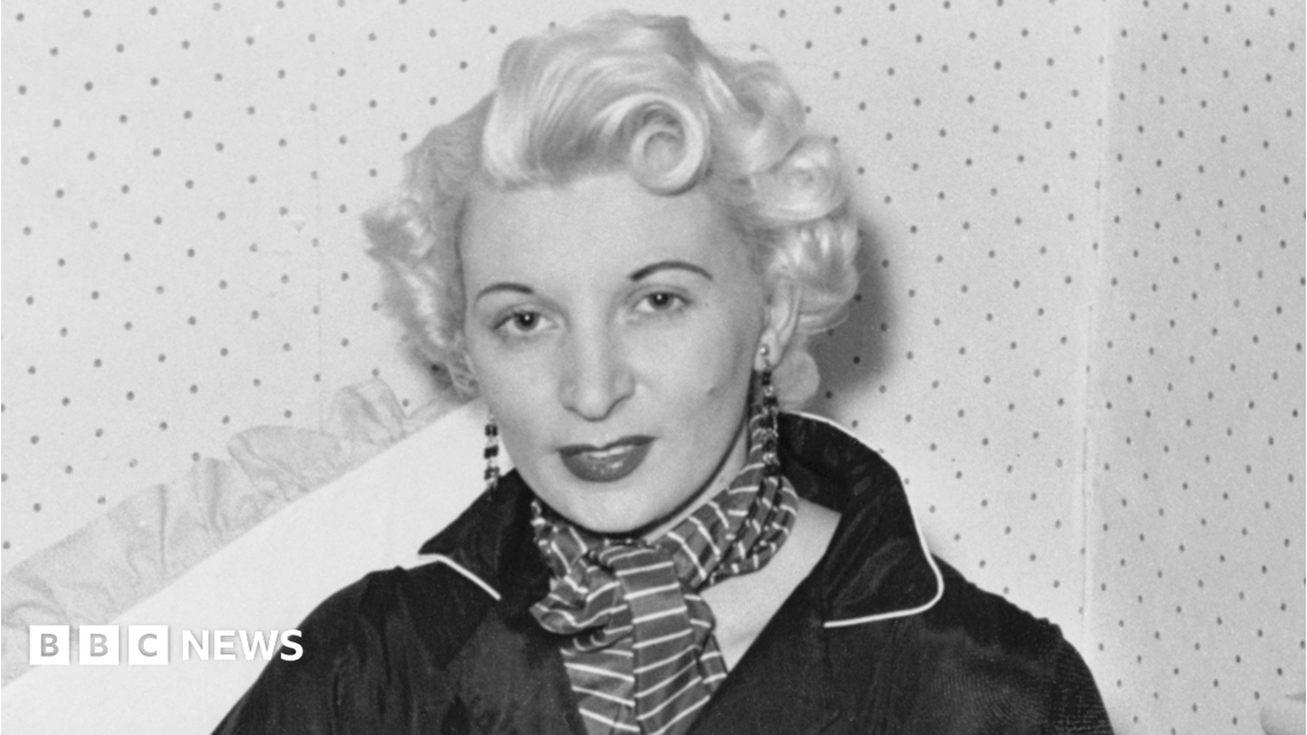 Ruth Ellis poses for a photograph - the black and white picture shows her with white-blonde hair, wearing long earrings, a striped scarf and a black shirt.