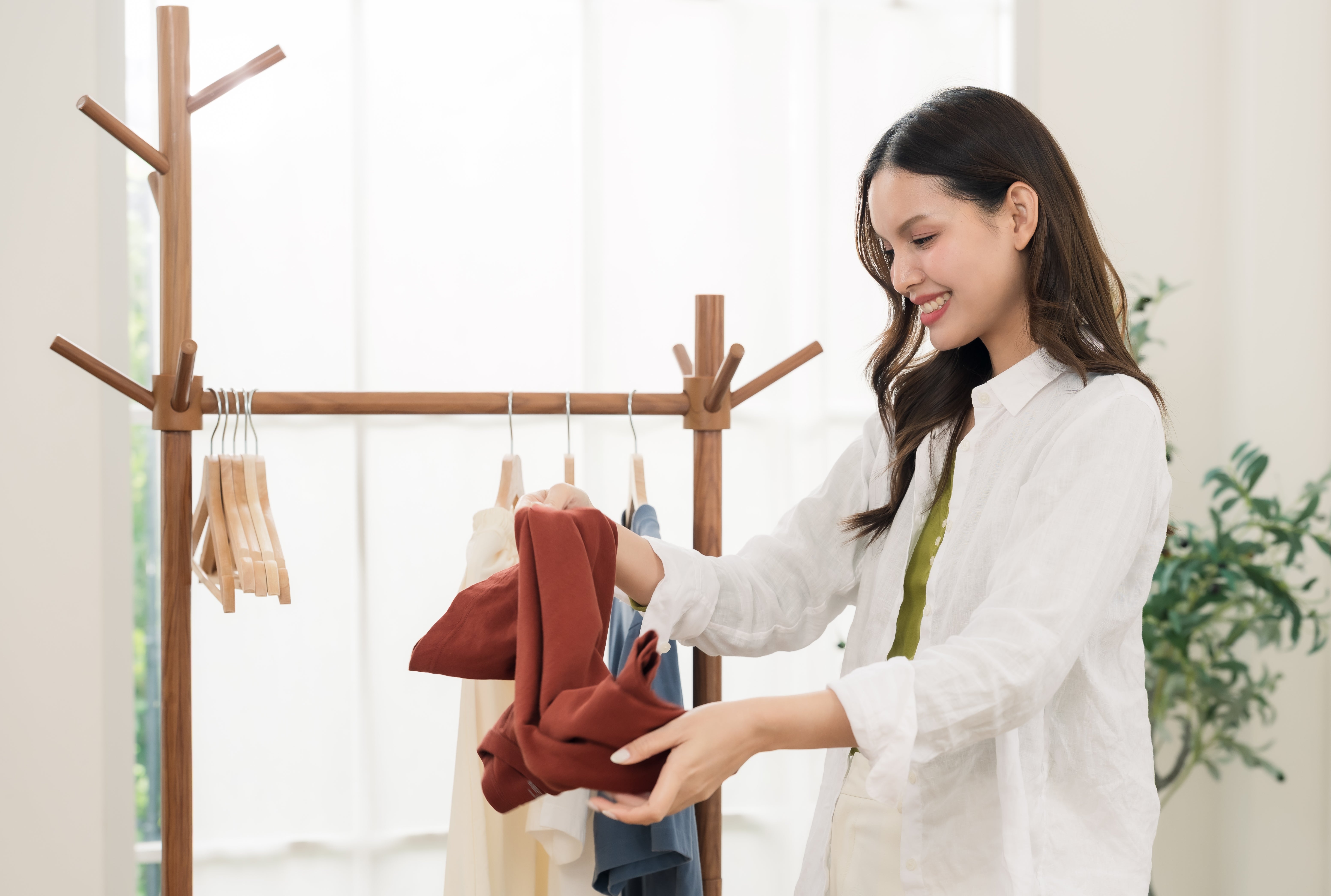 Person in a room examines clothes on a rack, possibly making work-related fashion choices