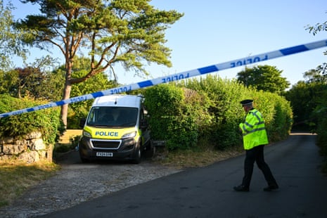 A police officer walking across a road cordoned off with police tape, with a van behind them