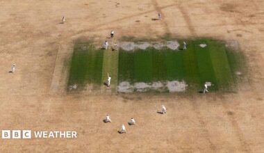 A cricket match on a yellow-brown, dry outfield with a green square
