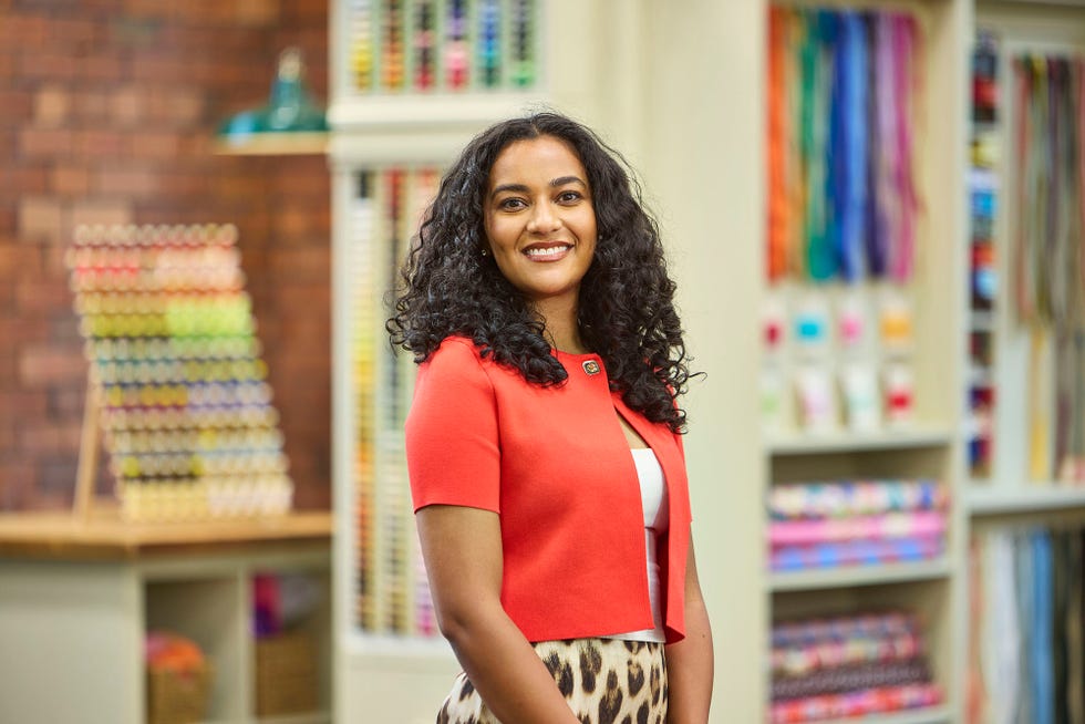 Heather contestant in The Great British Sewing Bee S12 2026 heather contestant in the great british sewing bee s12 2026 pictured in the mill, smiling in a red cardigan and animal print skirt